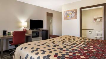 A hotel room with a bed, desk, chair, TV, and a bathroom visible through an open door.