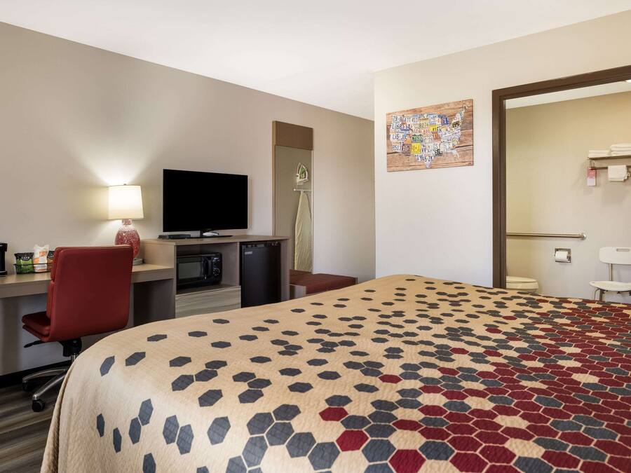 Habitación de hotel con cama, escritorio, silla, televisión y un baño visible a través de una puerta abierta.