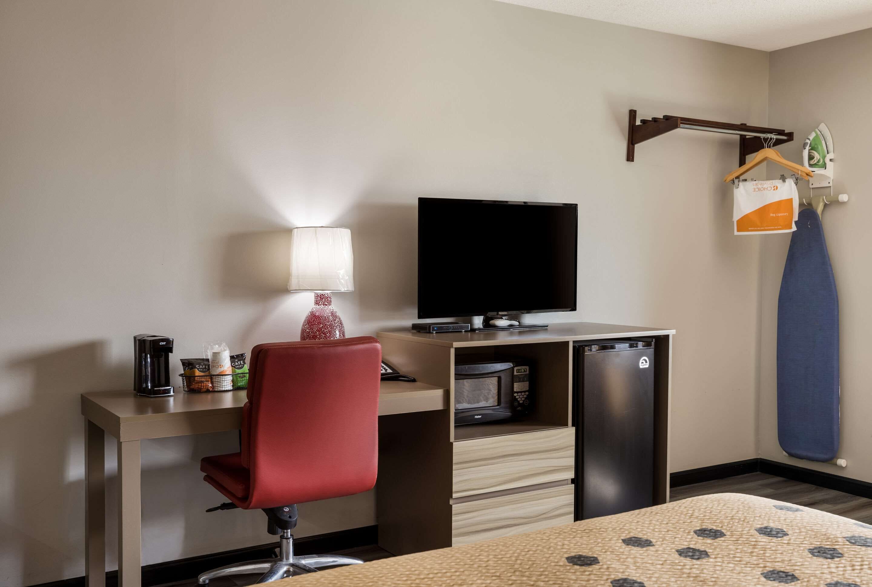Een hotelkamer met een bureau, een televisie, een magnetron en een kleine koelkast.