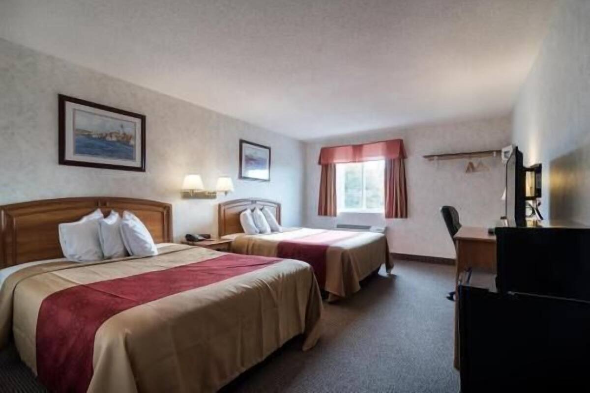 A hotel room with two beds, a desk, a chair, a TV, and a window with curtains.