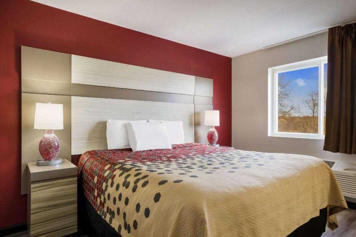 A hotel room with a large bed, two bedside tables, a headboard, and a window with a view.