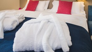 Una habitación de hotel con una cama bien hecha, dos almohadas, una colcha azul y dos lámparas de noche.