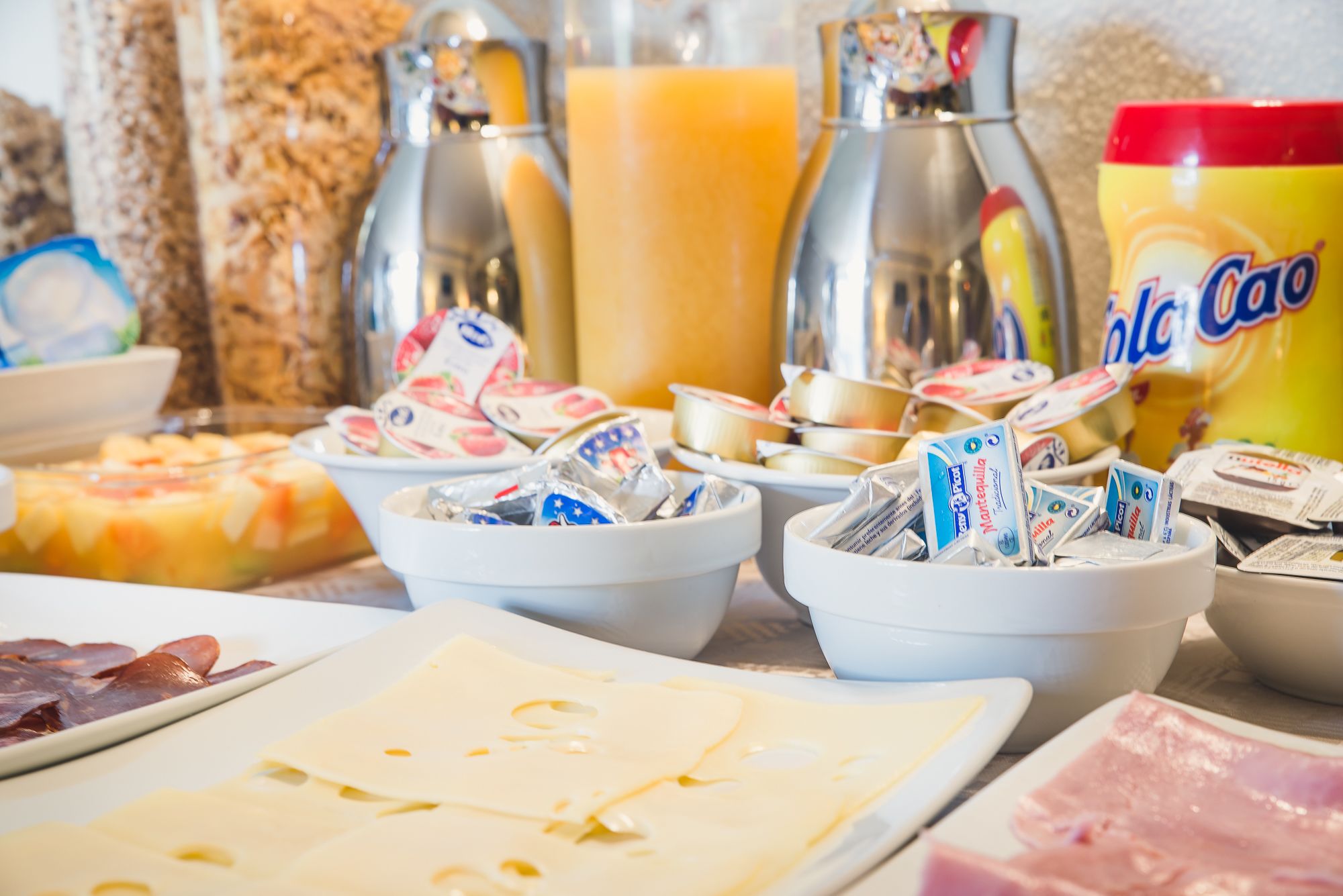 Une table de buffet proposant divers aliments, notamment du fromage, du jambon et des en-cas emballés.