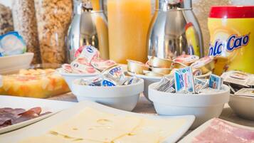 Une table de buffet proposant divers aliments, notamment du fromage, du jambon et des en-cas emballés.