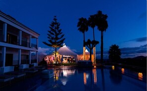 Un resort con piscina, una zona techada con palmeras y un edificio con balcones.
