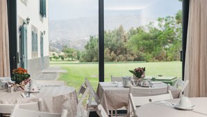 Comedor con mesas dispuestas para dos, con vistas a un paisaje verde a través de grandes puertas de cristal.