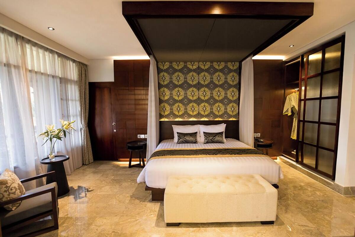 A modern hotel room with a large bed, a sitting area with a chair and a small table, and a large window with curtains.