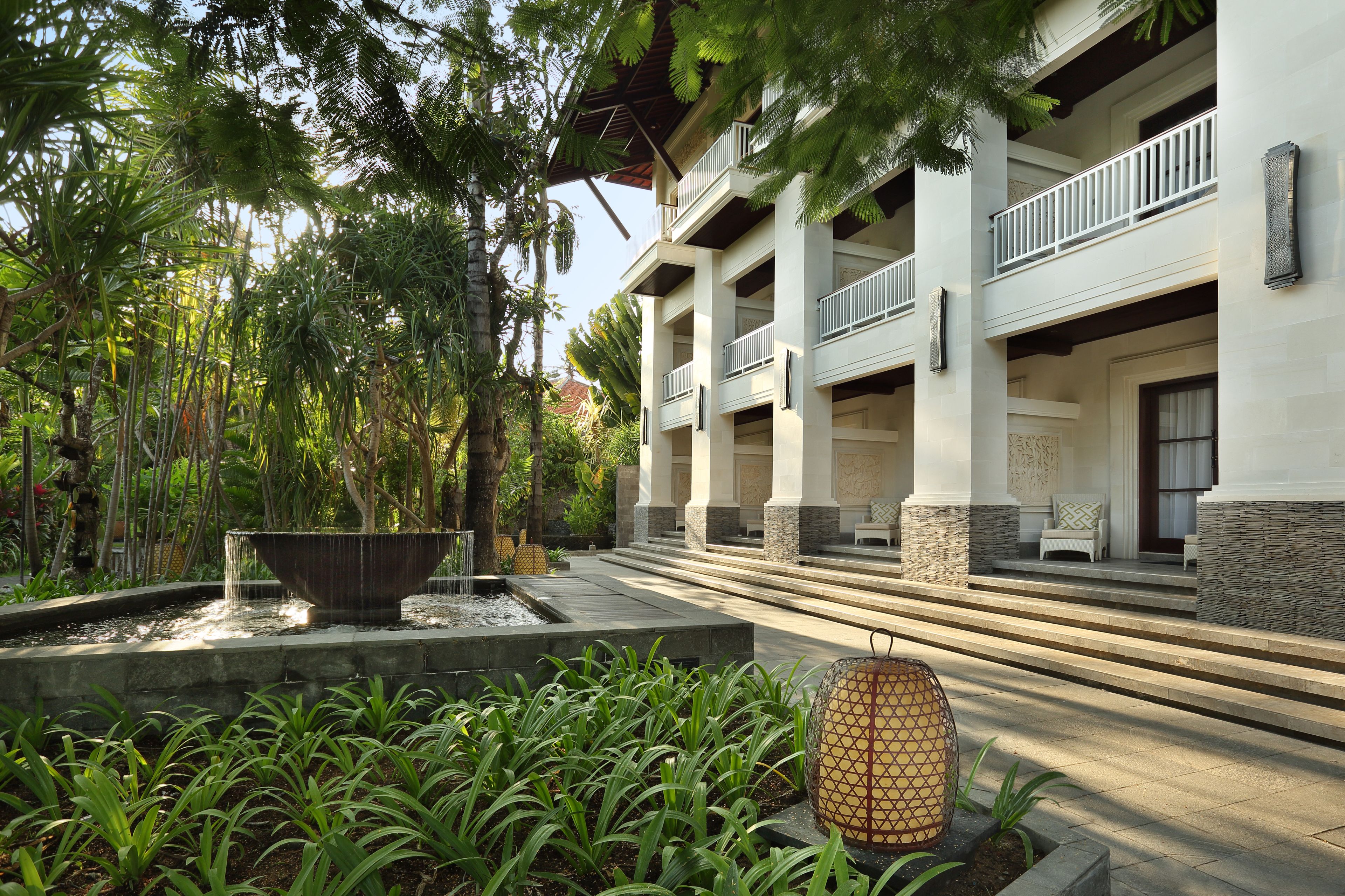 A hotel with a covered outdoor area, a large planter with plants, and a water feature.