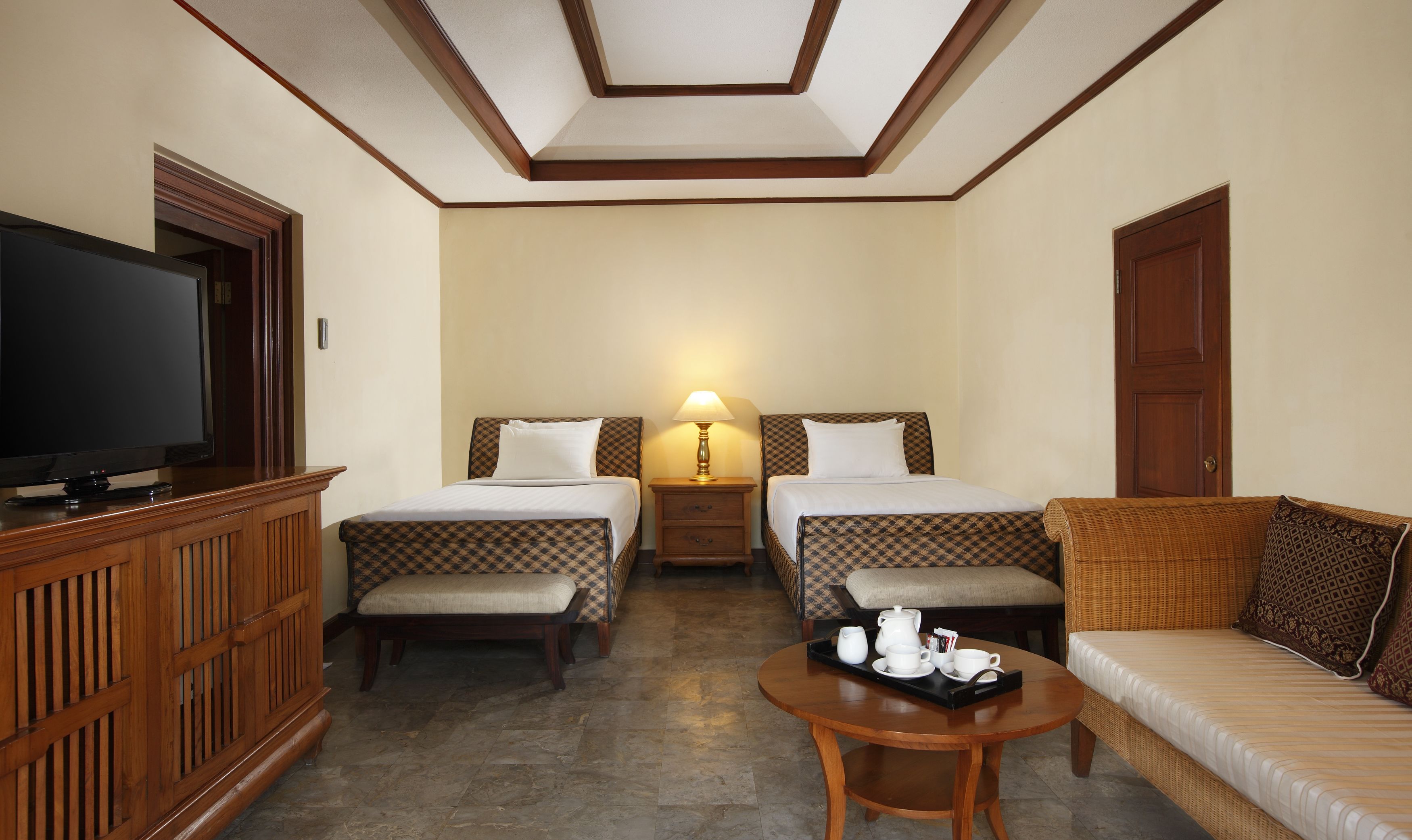 A hotel room with two beds, a television, a table with tea set, and a sofa.
