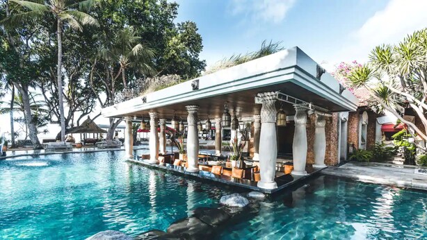 Eine Poolbar mit Steinsäulen und Sitzgelegenheiten, umgeben von einem tropischen Garten und einem klaren Pool.
