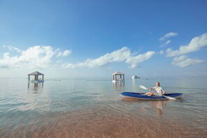 A tranquil water body with clear visibility, a person in a kayak, and two small structures on stilts.