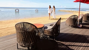 A beachside deck with wicker chairs and a table, overlooking the sea. - Puri Santrian (Denpasar)