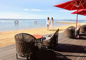 A beachside deck with wicker chairs and a table, overlooking the sea.