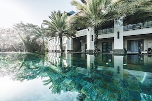 A hotel with a large swimming pool surrounded by palm trees, reflecting the architecture and greenery.