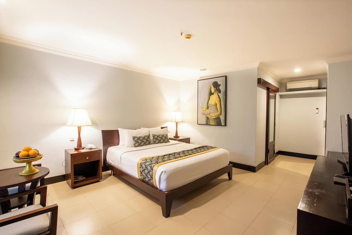 A hotel room with a bed, bedside lamps, a fruit bowl, a desk, and a television.