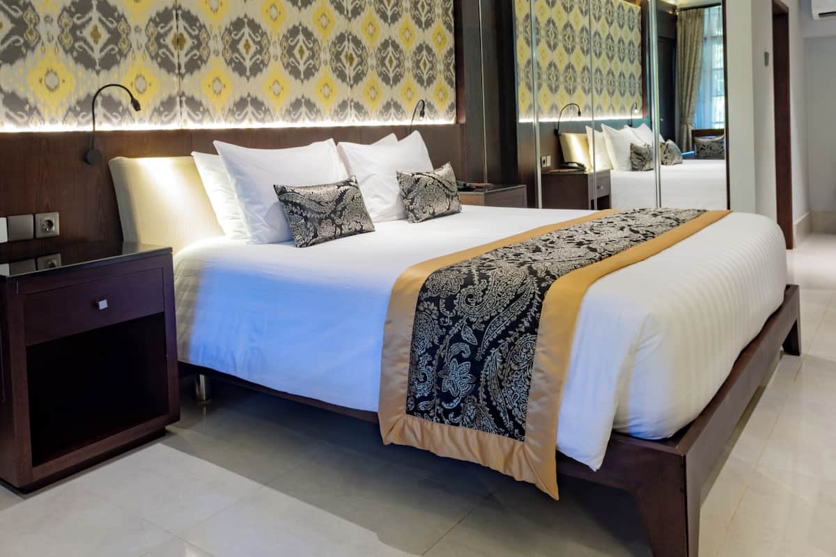 A modern hotel room with a large bed, a bedside table, a mirror, and patterned wallpaper.