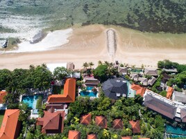 An aerial view of a coastal resort with a beachfront, swimming pools, and lush greenery.