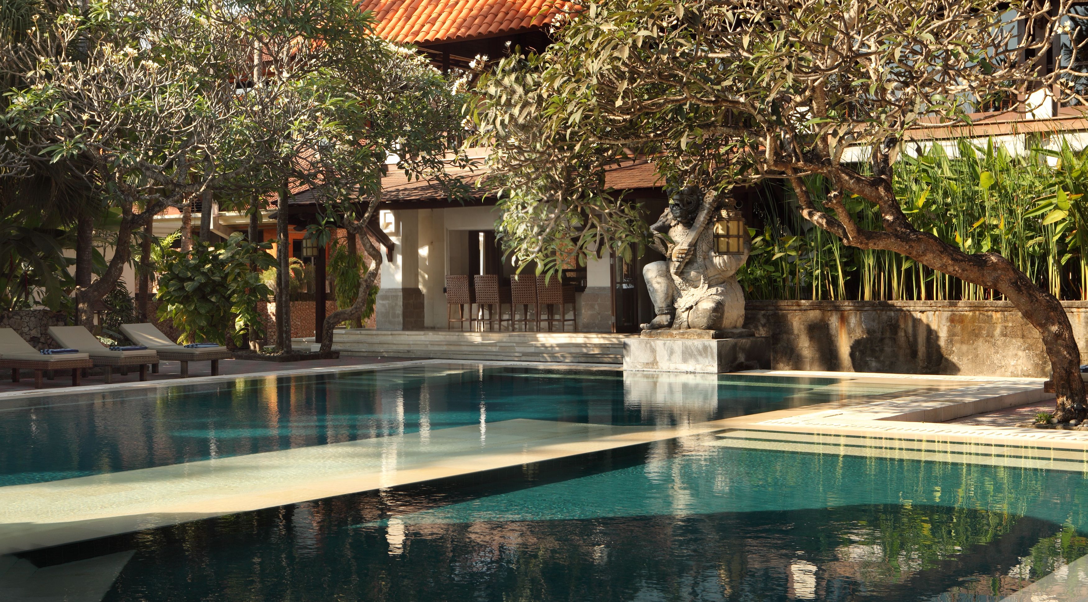 Piscina com espreguiçadeiras e uma estátua de pedra.