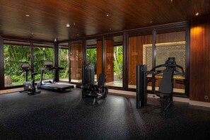 A gym with cardio machines, weightlifting equipment, and large windows offering a view of greenery.