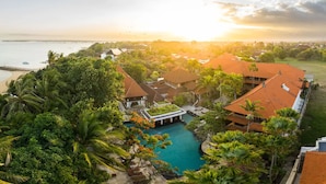 Ein Resort mit Schwimmbad, umgeben von üppiger Vegetation und Palmen, mit Blick auf einen Strand und das Meer.