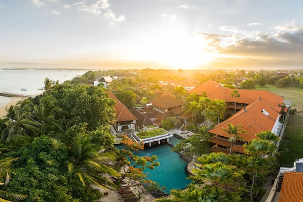 A resort with a swimming pool surrounded by lush greenery and palm trees, overlooking a beach and ocean. - Puri Santrian (Denpasar)