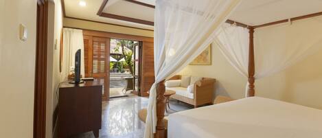 A bedroom with a four-poster bed, a wooden dresser, and a seating area with a wicker sofa.