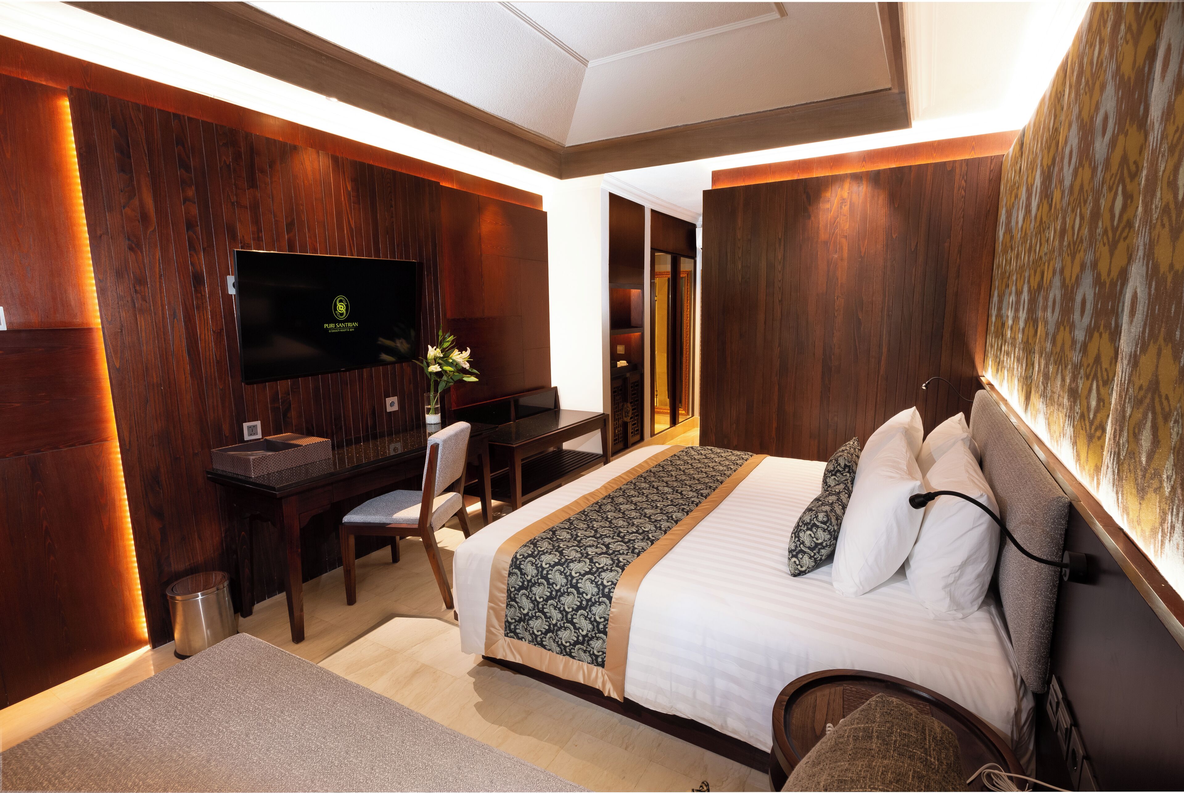 A hotel room with a large bed, a desk with a TV, and a seating area.