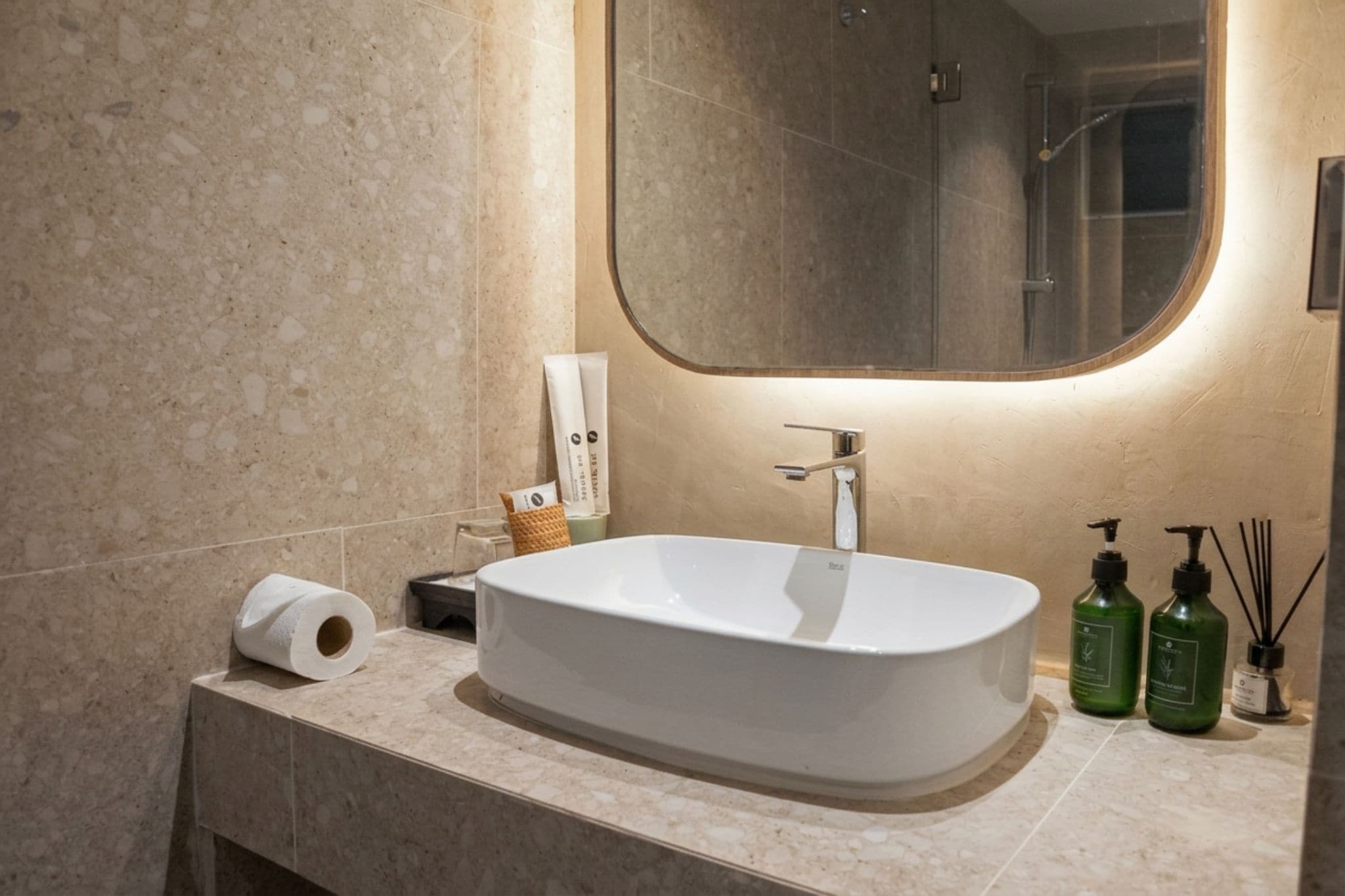 A bathroom with a freestanding sink, a mirror, a towel dispenser, and a toilet paper roll.