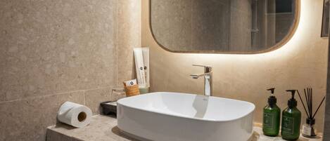 A bathroom with a freestanding sink, a mirror, a towel dispenser, and a toilet paper roll.