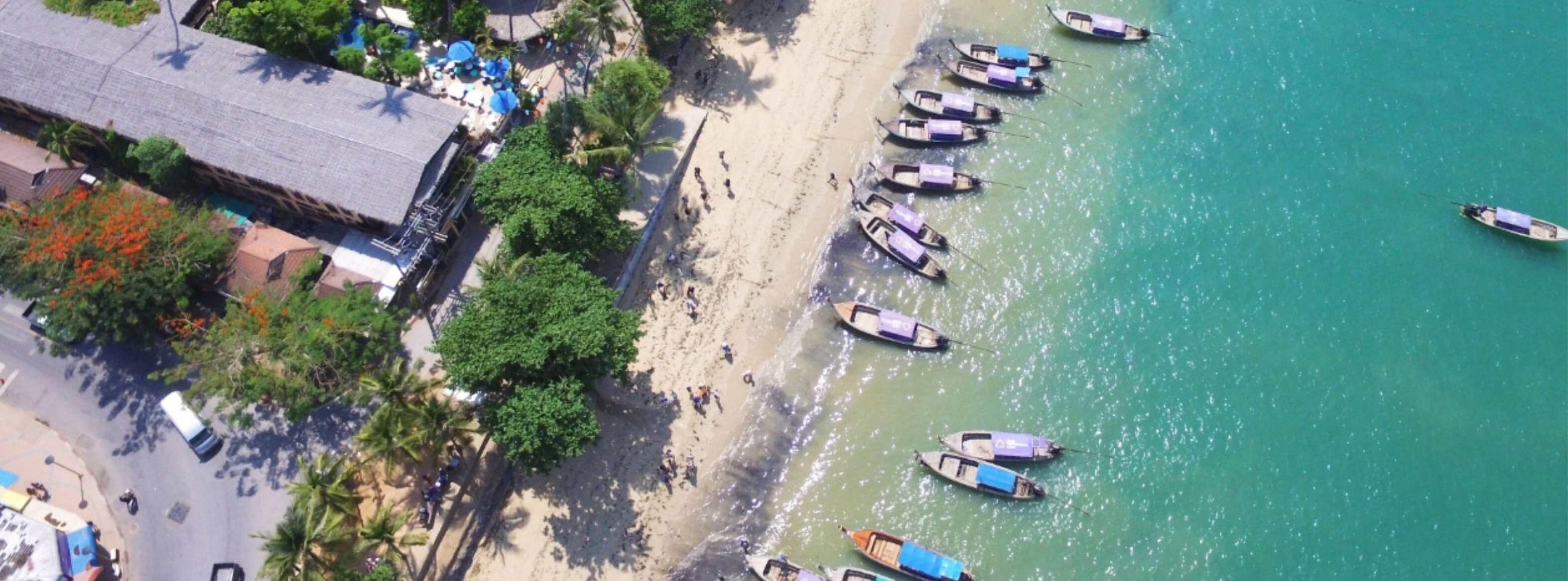 Une plage où plusieurs bateaux sont amarrés le long du rivage, et un bâtiment à toit de chaume situé à proximité.