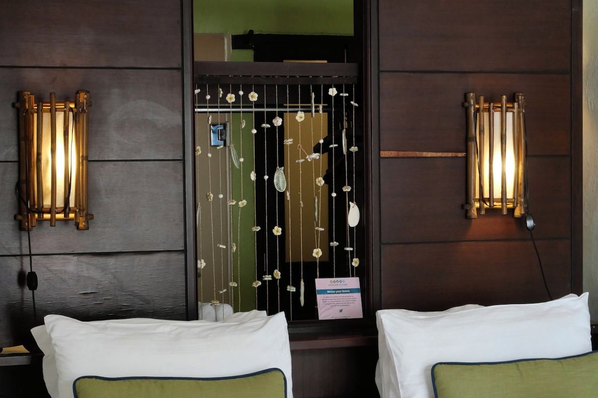 Een hotelkamer met twee bedden, een bedspreide met groene bloemen en wandlampen.