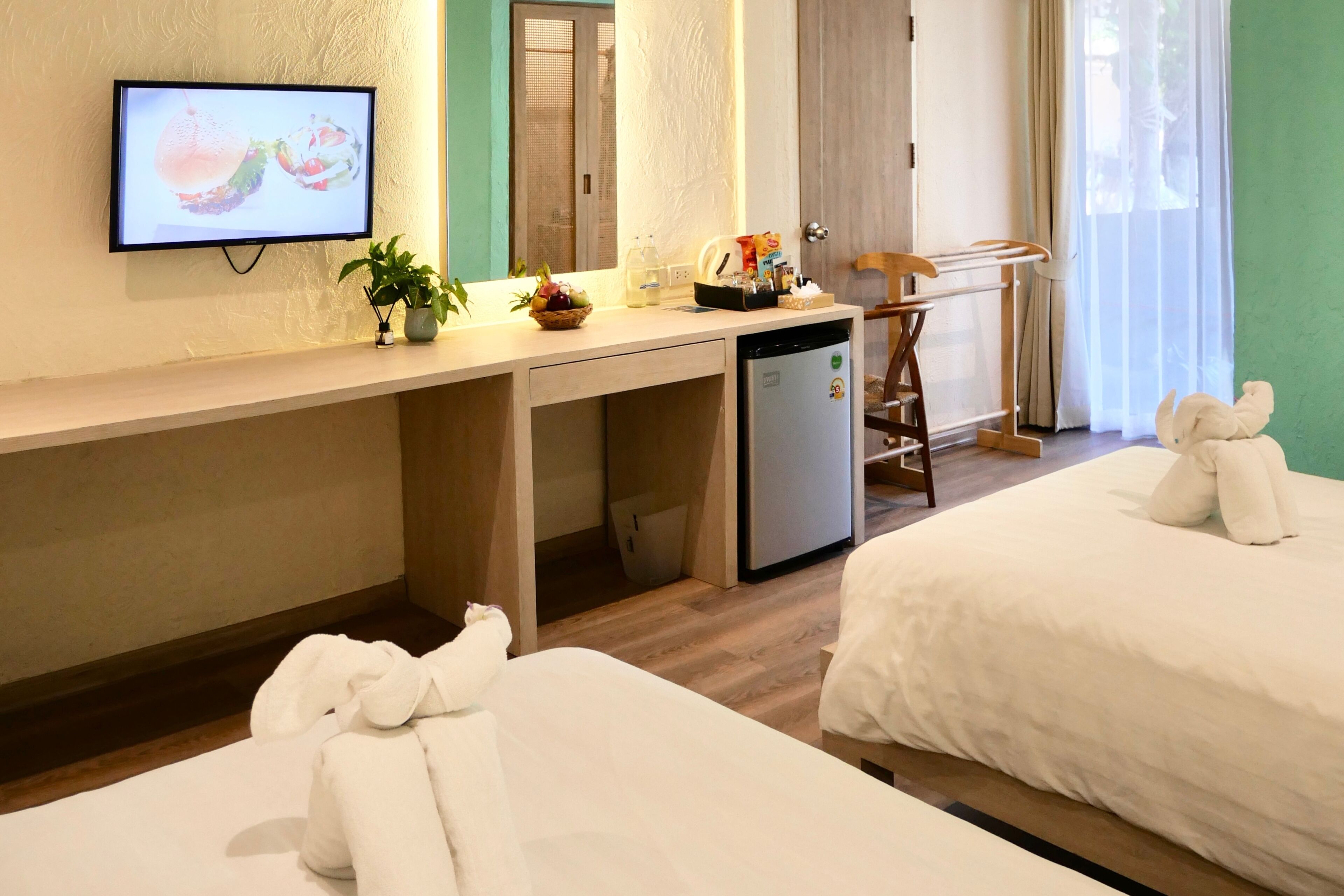 A hotel room with a bed, a desk with a computer, a television, and a window with curtains.