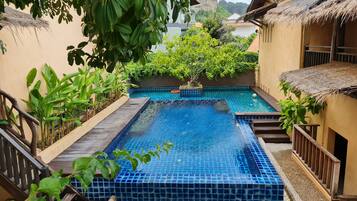 Piscina con azulejos azules, rodeada de plantas y una terraza de madera.