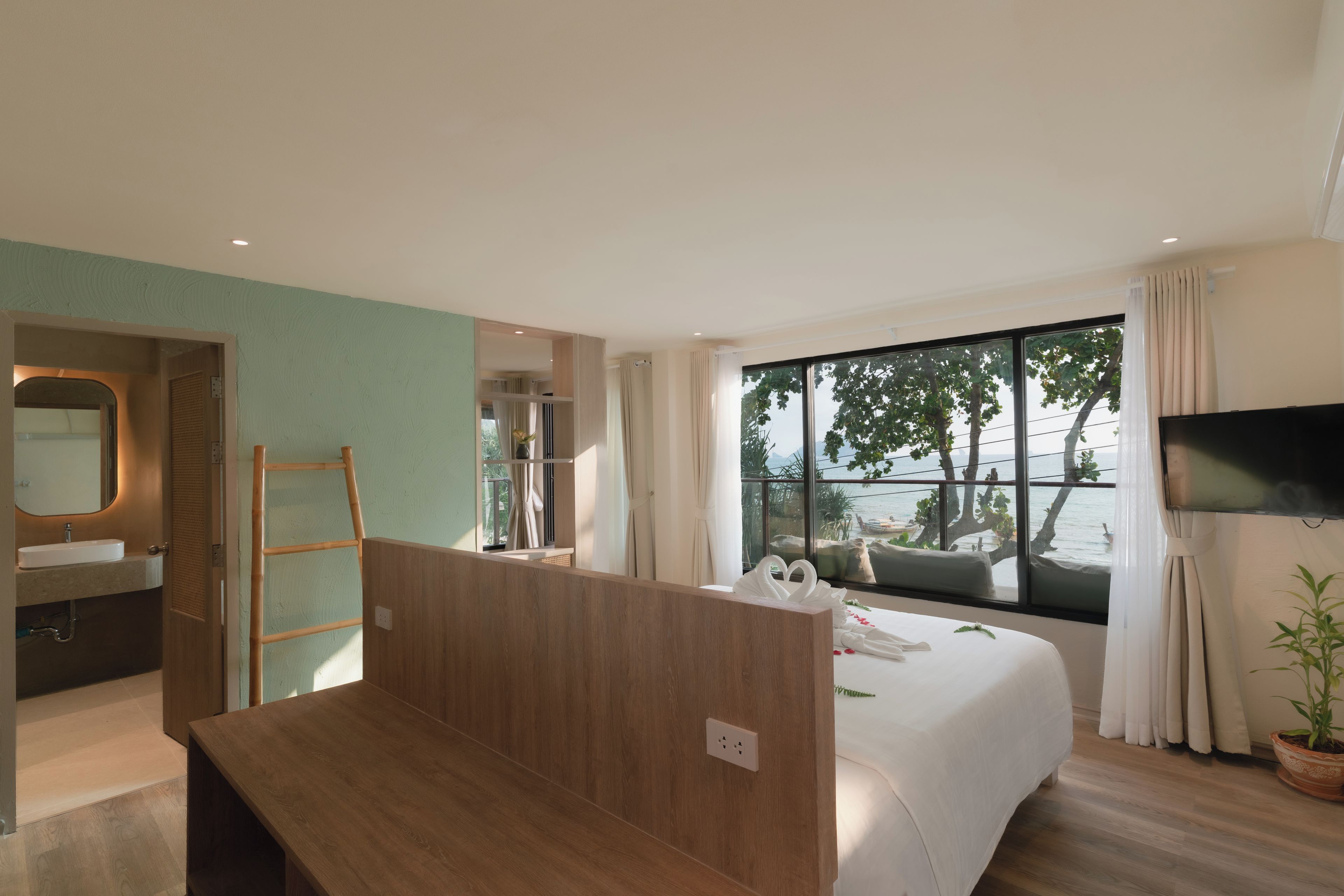 Habitación de hotel con cama, televisor, ventana con vista al mar y baño con lavabo y espejo.