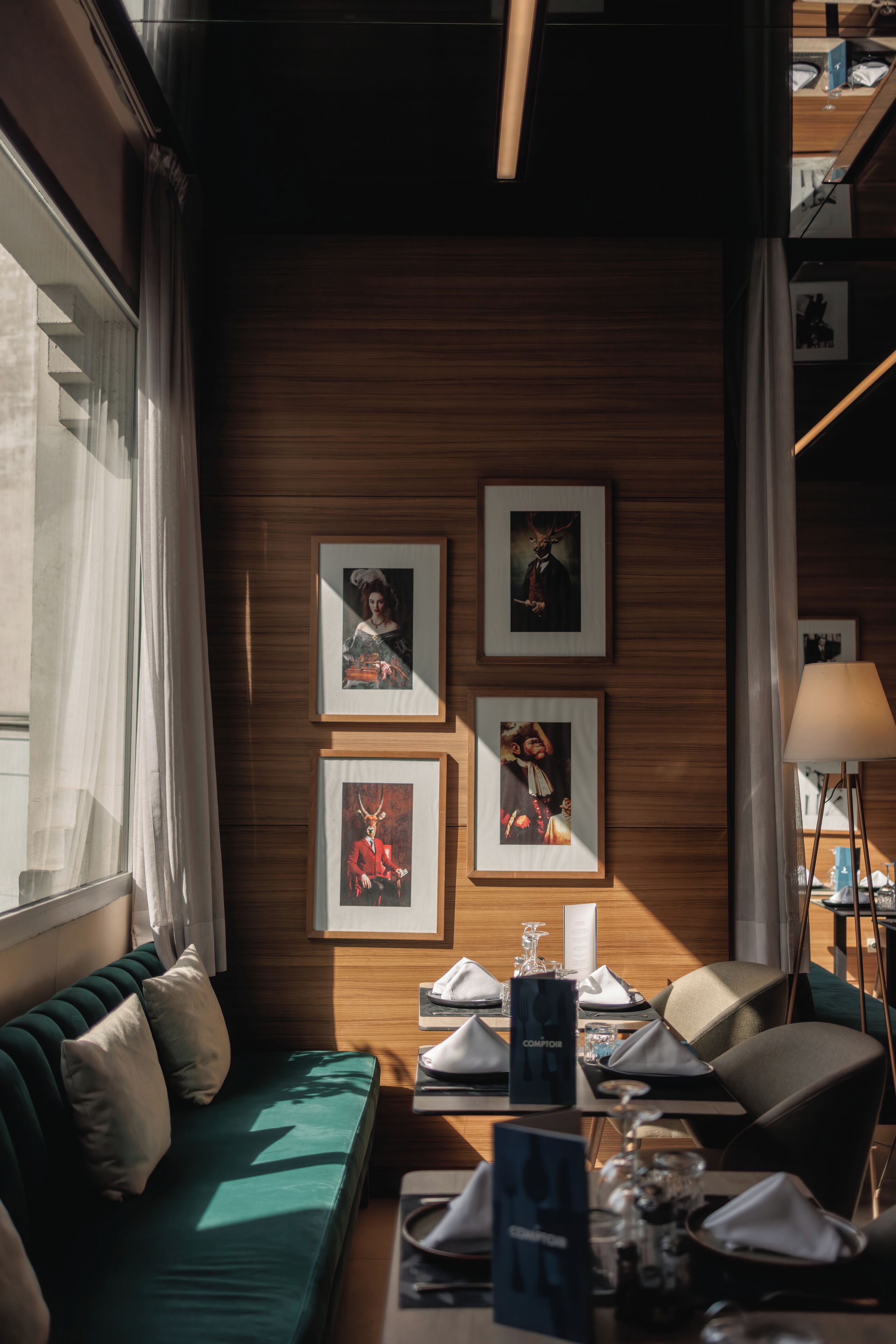 A cozy room with a wooden wall, a green sofa, and a dining table set with a lamp and framed pictures.