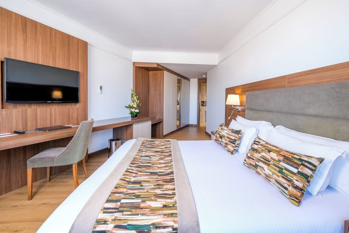 A hotel room with a large bed, a desk, a chair, a television, and a lamp.