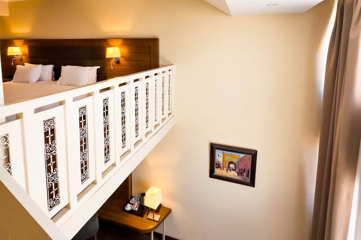 A hotel room with a bunk bed, a desk with a lamp, a framed picture on the wall, and a window with curtains.