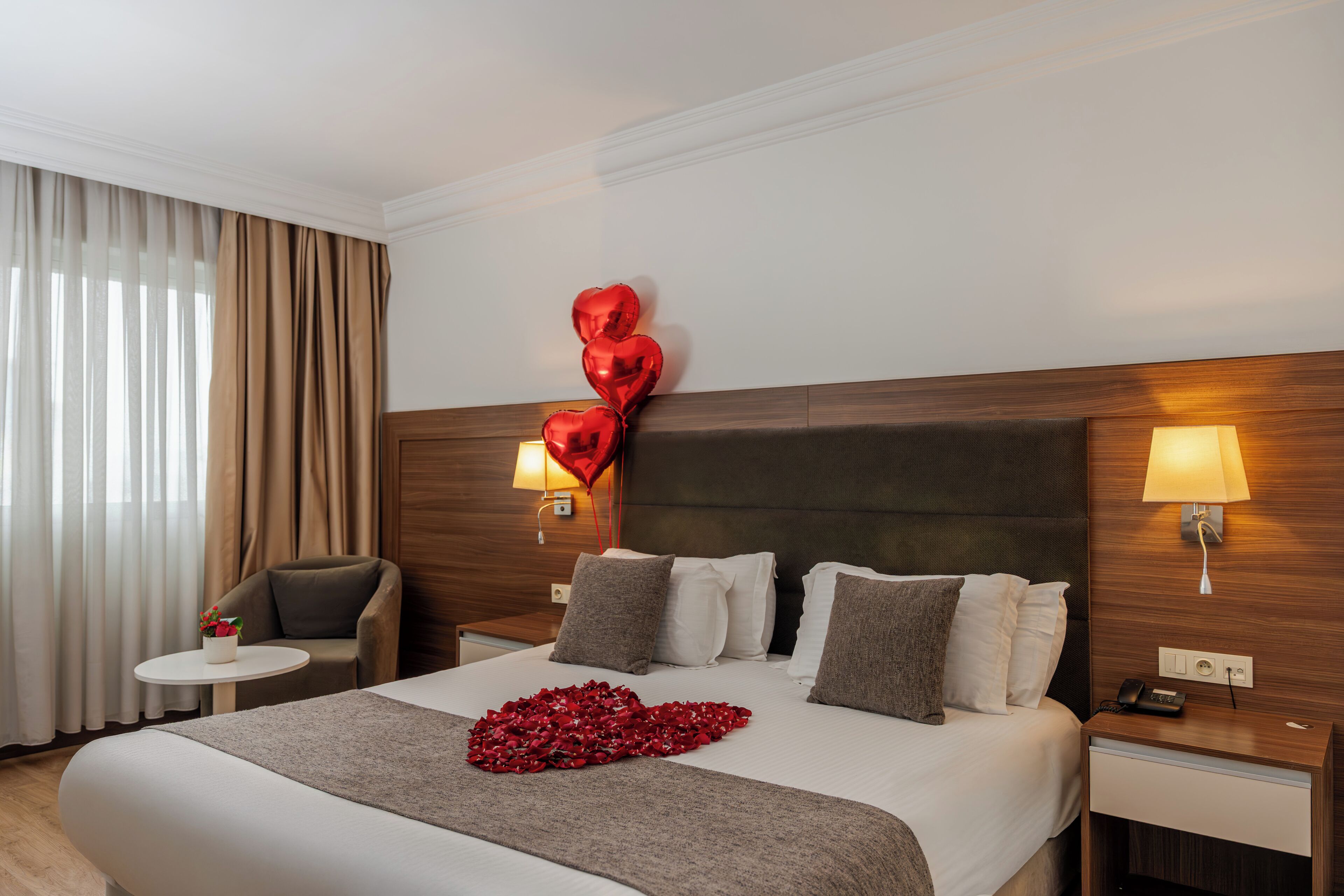 Quarto de hotel com cama, abajures, uma cadeira e uma mesa pequena.