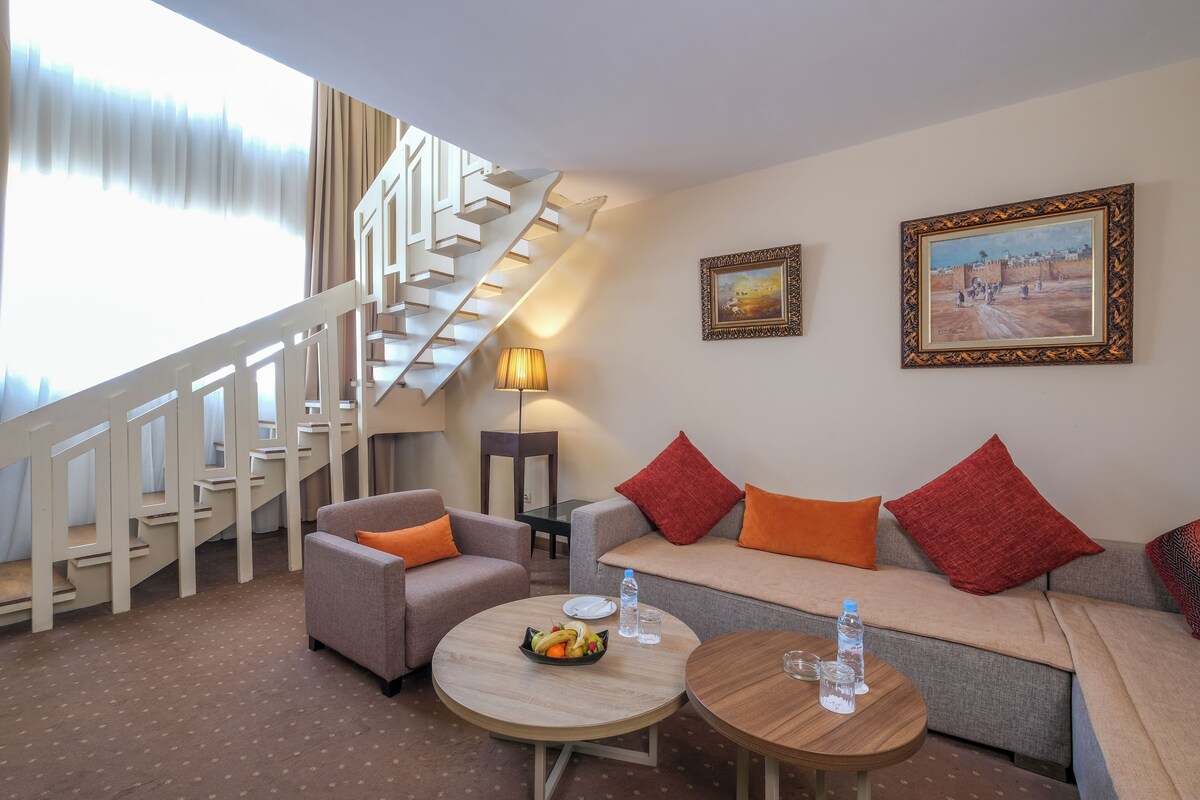 Habitación de hotel con escalera, un conjunto de sofás, una mesa de comedor y dos cuadros en la pared.