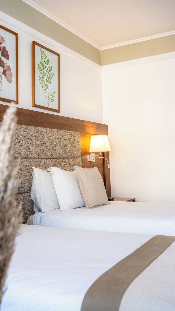 Una habitación de hotel con una cama grande, un cabecero con diseño texturizado, una lámpara de noche y dos grabados botánicos enmarcados en la pared.