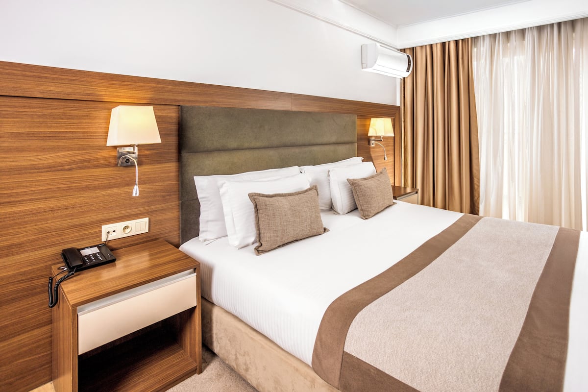 A hotel room with a wooden headboard, a bedside table with a lamp, a phone, and a bed with white and brown bedding.