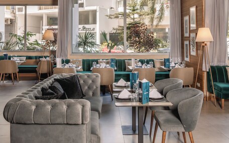 A modern interior with a dining area, sofas, and a large window offering a view of the outdoors.