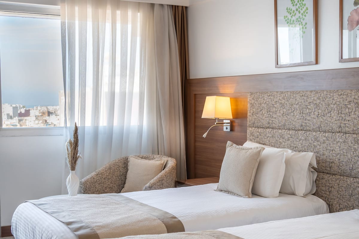 A hotel room with two beds, a city view, a lamp, and a framed picture on the wall.