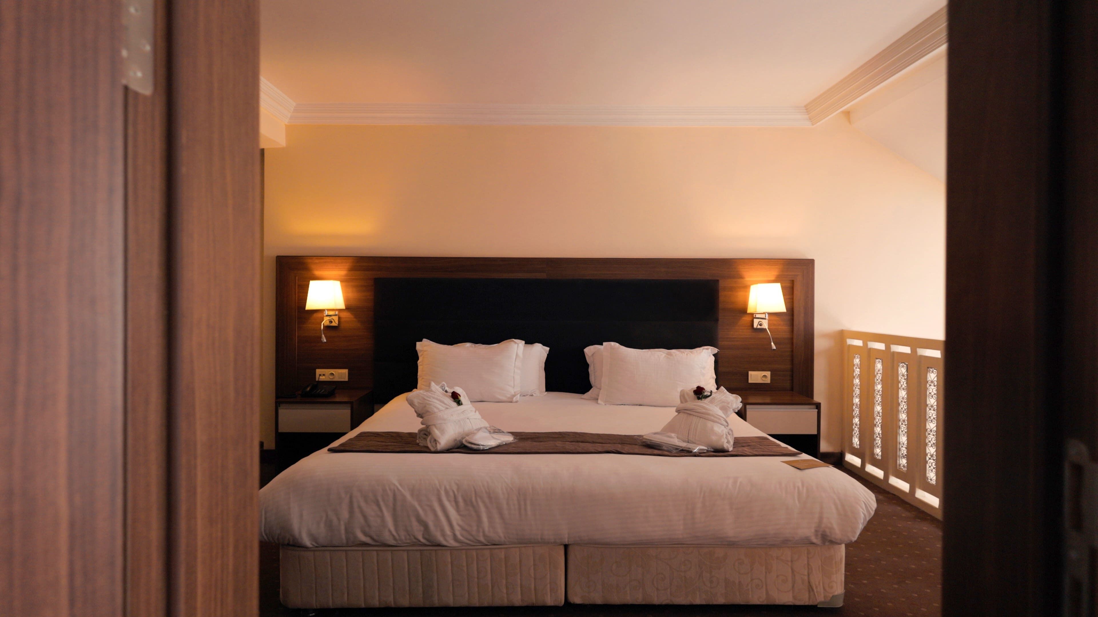 Quarto de hotel com uma cama grande, duas luminárias de cabeceira e uma cabeceira de madeira.