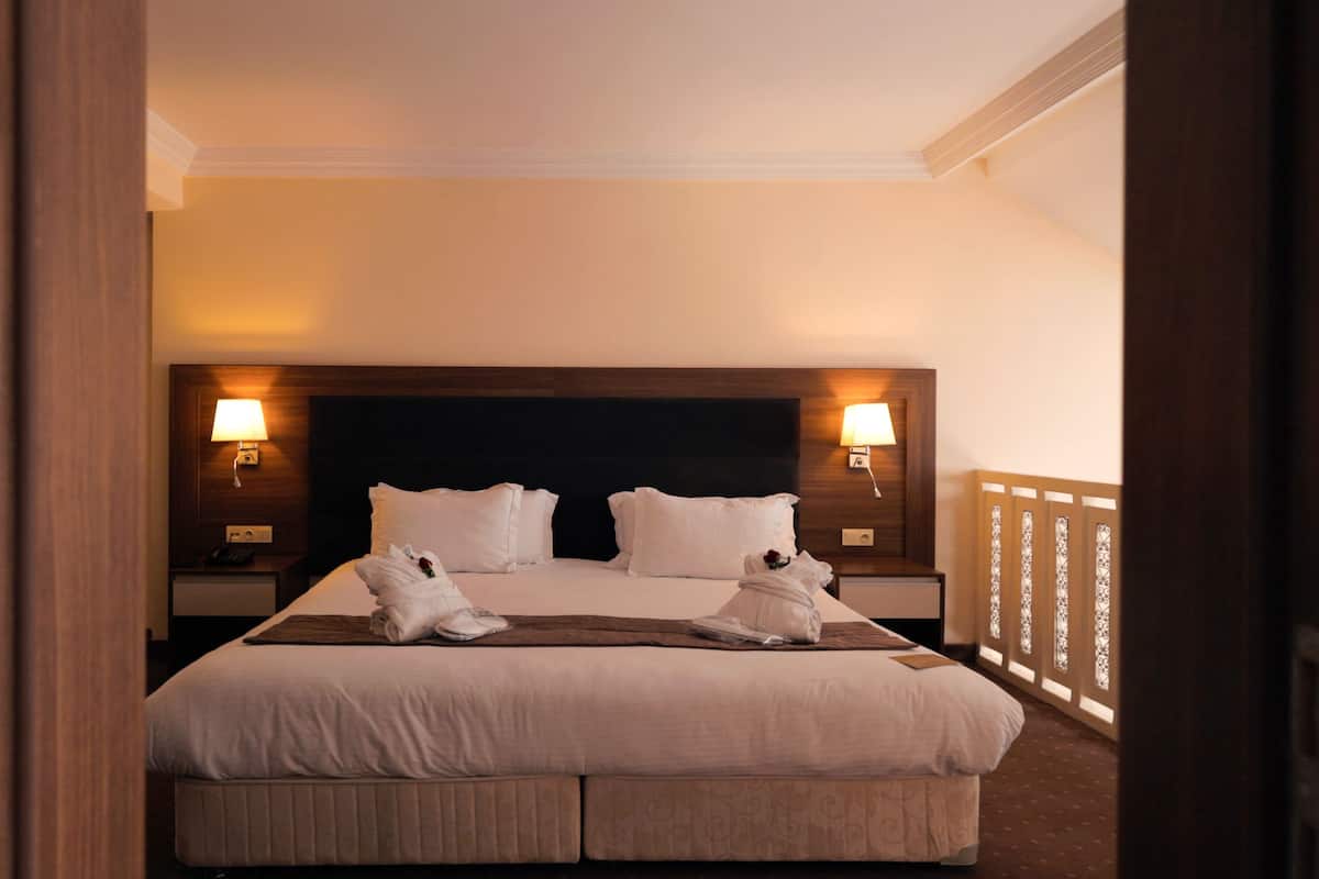 Quarto de hotel com uma cama grande, duas luminárias de cabeceira e uma cabeceira de madeira.