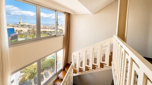 Un interior de rascacielos con amplios ventanales que ofrecen vista panorámica de la ciudad, una escalera con barandales decorativos y un cielo despejado.