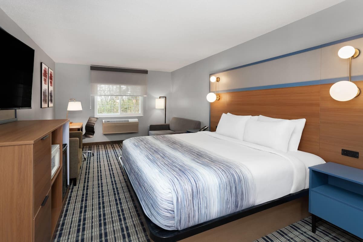 A hotel room with a bed, bedside tables, a desk, a chair, a TV, and a window with blinds.