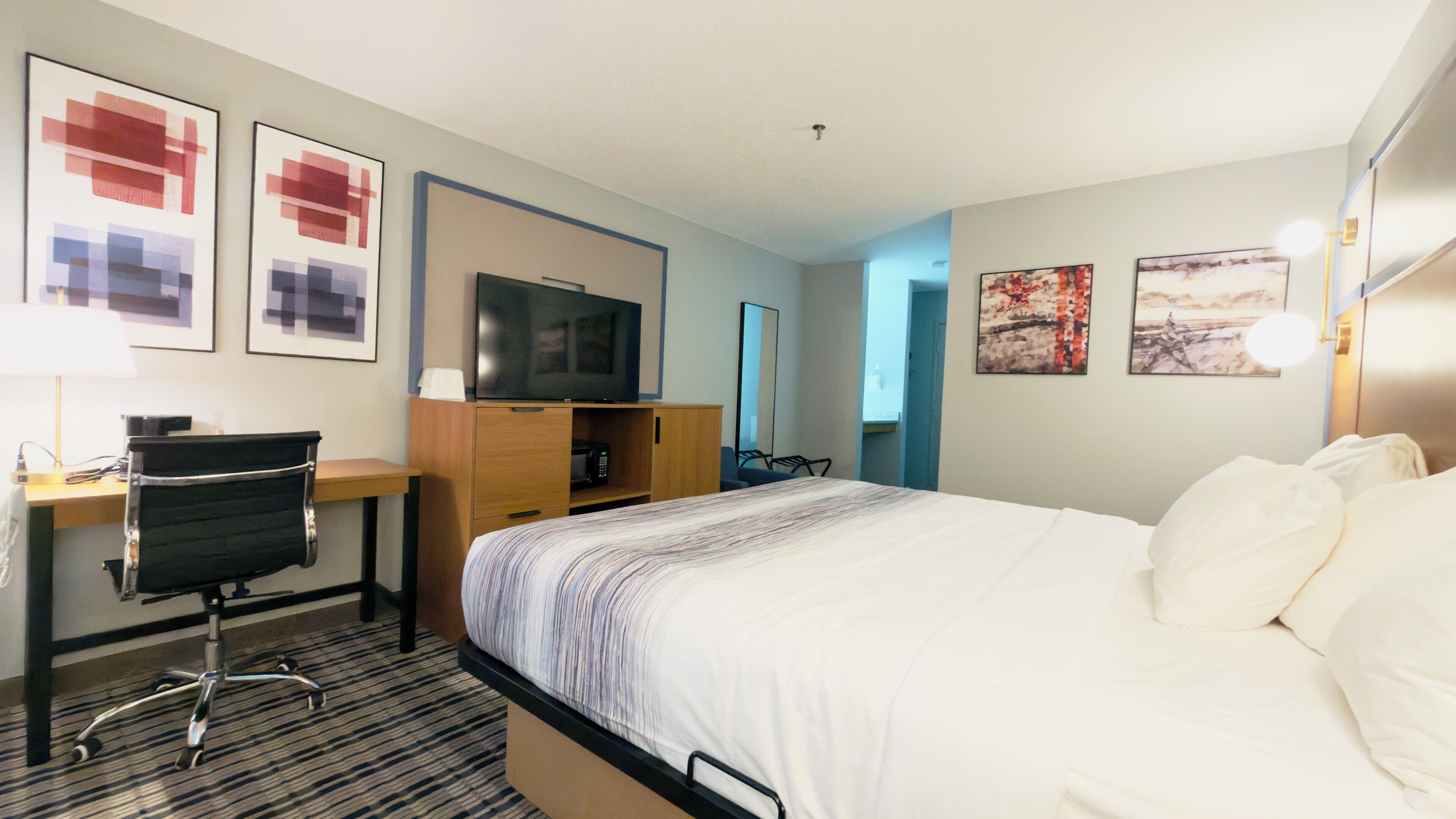Ein Hotelzimmer mit Bett, Schreibtisch, Stuhl, Fernseher und Bildern an den Wänden.