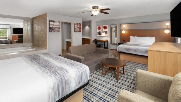 A hotel room with a large bed, a sofa, a small table, a desk, a ceiling fan, and a TV. - AmericInn by Wyndham Lake Mills (Lake Mills)