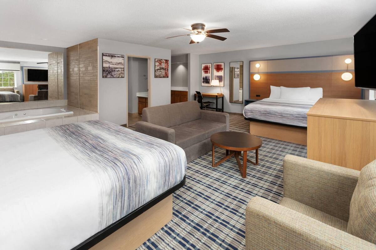 A hotel room with a large bed, a sofa, a small table, a desk, a ceiling fan, and a TV.